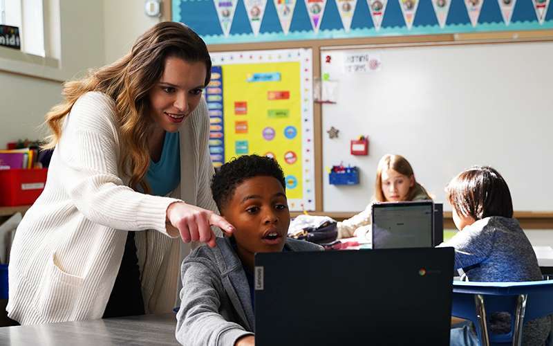 A teacher pointing to a screen with a student following along