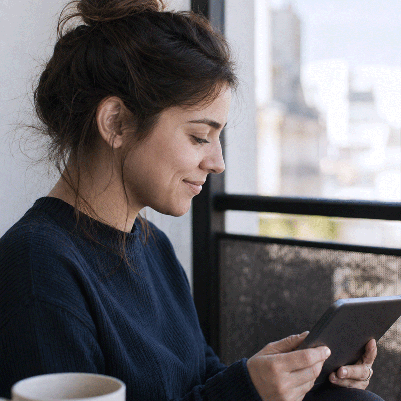 A young woman reading a tablet on a terrace with a cup of coffee